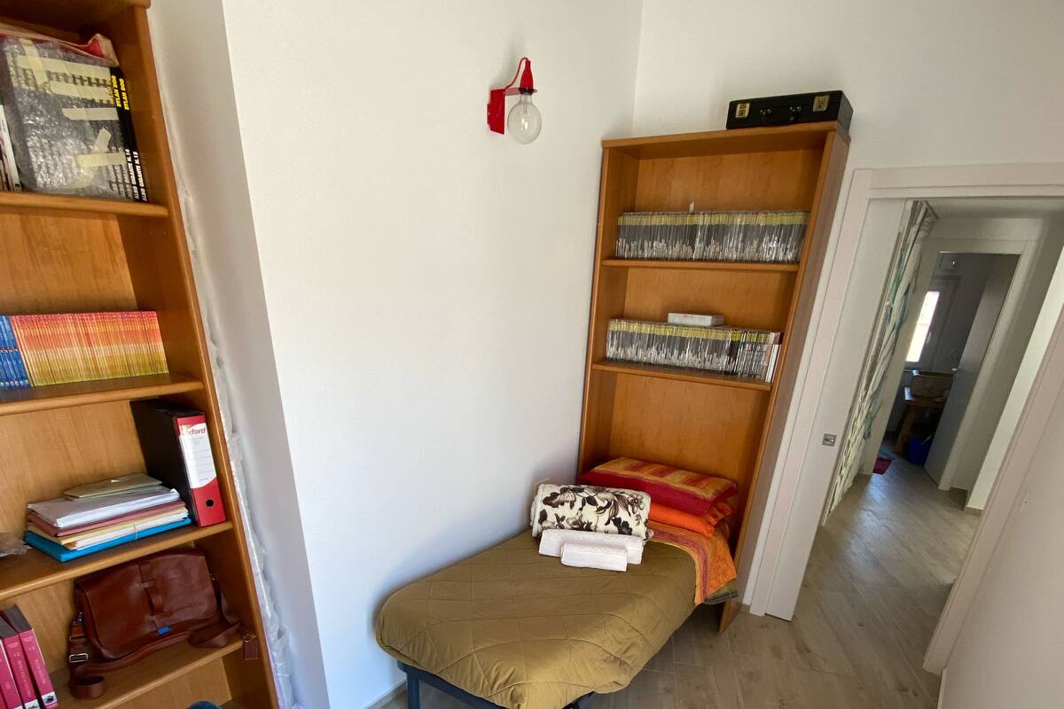 Habitación pequeña con cama, escritorio, silla, estantería e iluminación fijada a la pared.