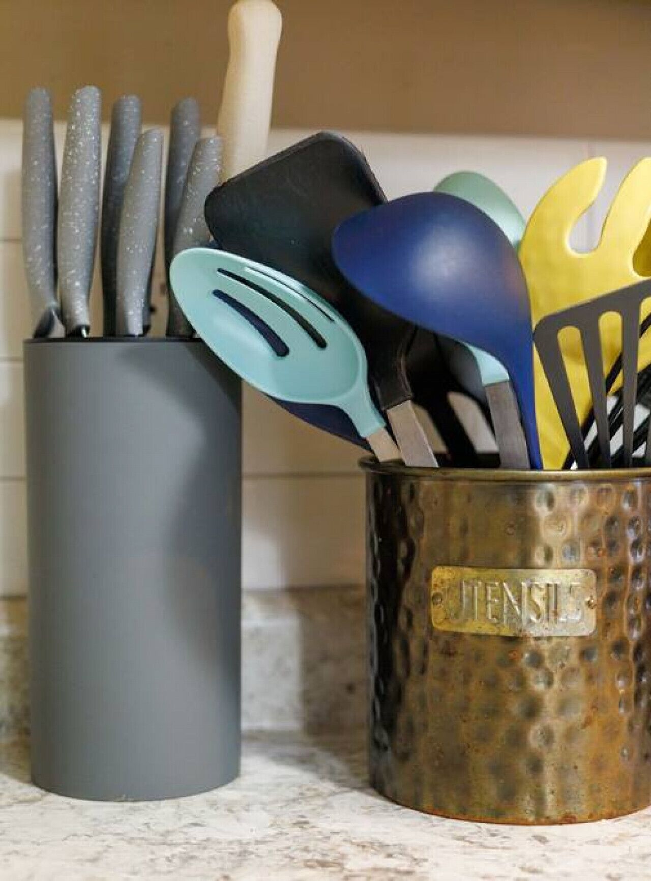 Un porte-ustensiles de cuisine contenant divers outils, notamment des spatules et une râpe, posé sur un plan de travail en marbre.