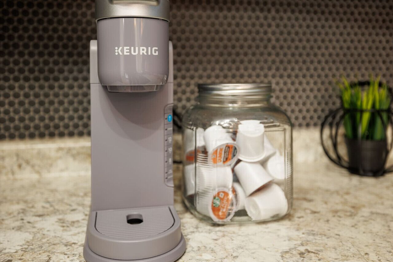 A Keurig coffee maker on a kitchen counter next to a jar filled with coffee pods.
