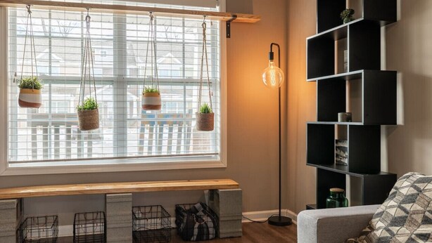 Una habitación con un ventanal grande, un banco, una lámpara de pie y una estantería.