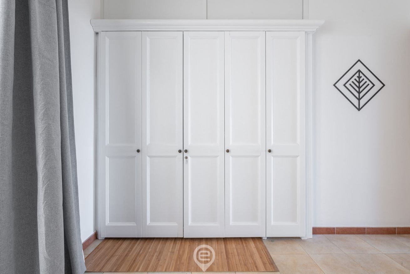 A white wardrobe with three doors and a small decorative symbol on the wall.