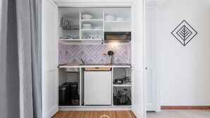 Une cuisine de taille réduite avec des meubles blancs, un petit réfrigérateur et un four à micro-ondes.