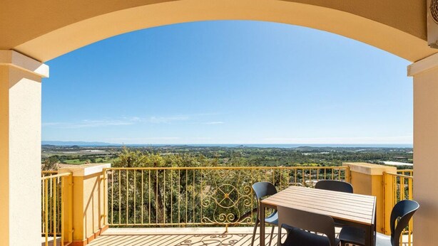 Un balcon avec une table et des chaises, une rambarde jaune et une vue sur un paysage verdoyant.
