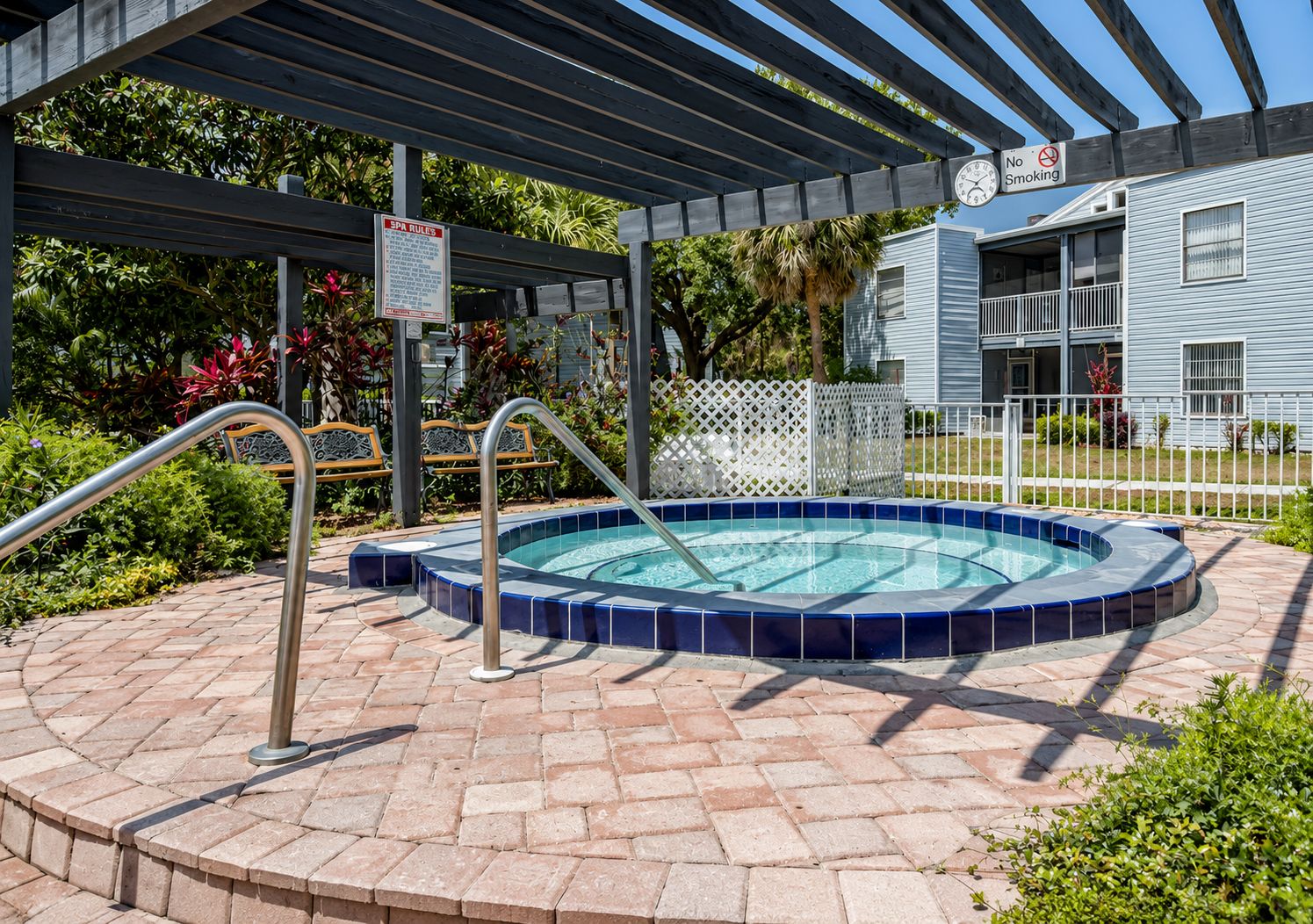 A swimming pool with a tiled edge, a metal handrail, and a covered area with a pergola.