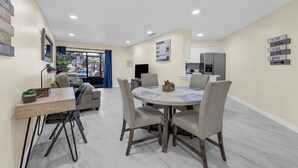 A modern living room with a round dining table, comfortable seating, a sofa, and a kitchen area in the background. - 3919 Orlando Vacational Apartment (Orlando)
