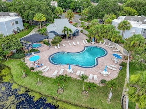 A swimming pool with a unique shape, surrounded by lounge chairs and umbrellas, set in a lush green environment with palm trees. - 3919 Orlando Vacational Apartment (Orlando)