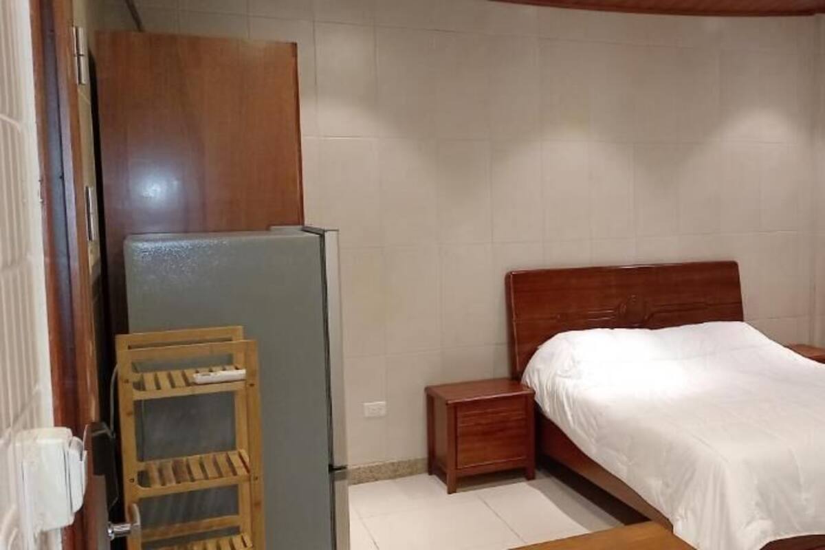 Ein Schlafzimmer mit einem Einzelbett, einem Holzkopfteil, Nachttischen, einer kleinen Holzablage und einem Kühlschrank.