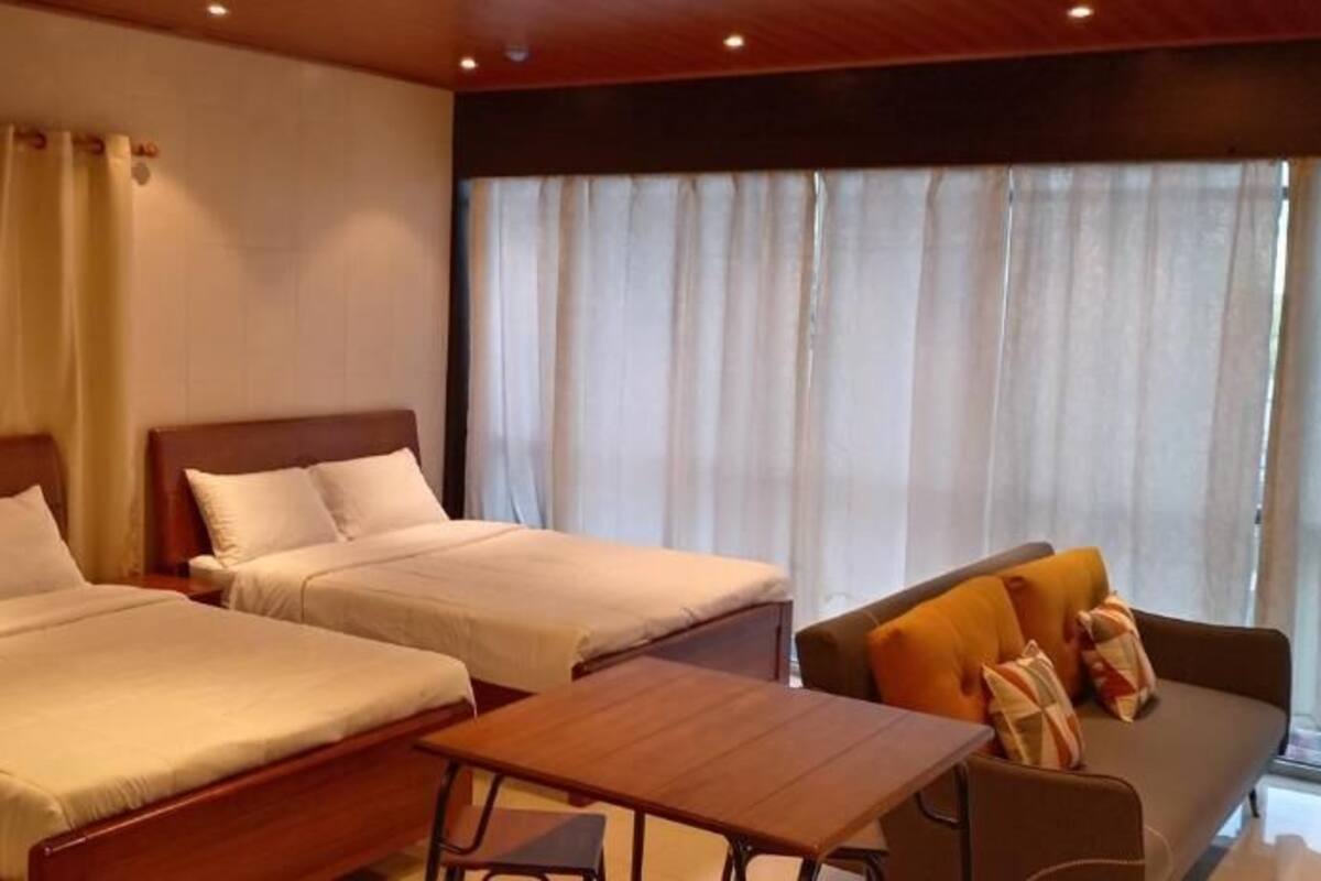 Ein Hotelzimmer mit zwei Betten, einem Sofa, einem Holztisch und großen Fenstern mit Vorhängen.