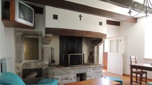 A living room with a stone fireplace, a television, and teal sofas. - L'oustal Bergounhou (Le Bas-Ségala)