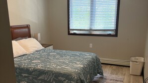 Une chambre à coucher avec un lit, une fenêtre avec des stores, un petit radiateur et un tapis à motifs.