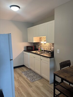 A compact kitchen with white cabinets, a microwave, a sink, and a dining area with a table and chair.