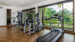 Un gimnasio con cintas de correr, elípticas y equipo de pesas, ventanas amplias con vistas a la vegetación.