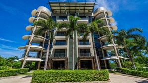 Un edificio moderno de varios pisos con un atrio central, rodeado de palmeras y abundante vegetación.