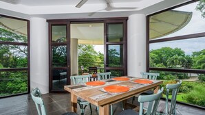 Un comedor con una mesa y sillas de madera, ventanas amplias y vista a zonas verdes.