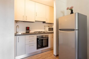 Uma cozinha moderna com armários brancos, uma geladeira de aço inoxidável, micro-ondas, fogão a gás e forno.