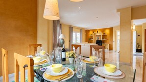 A dining area with a glass table set for a meal, chairs, and a modern kitchen in the background.