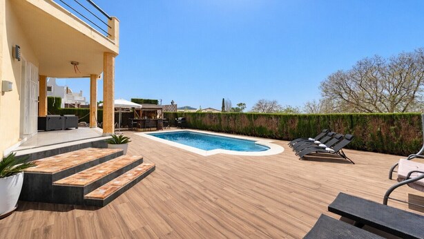 A swimming pool with a wooden deck, lounge chairs, and a bar area.