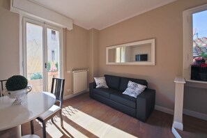 Une pièce comprenant une table à manger, un canapé, un radiateur et une fenêtre donnant sur l’extérieur.