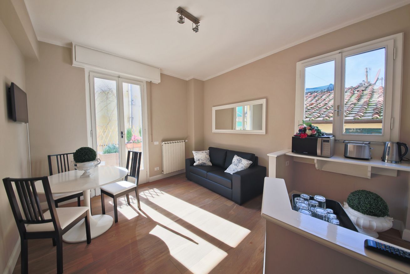 A spacious living area with a dining table, chairs, a sofa, and a kitchen area with appliances.