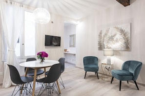 Un salon moderne avec une table à manger ronde, deux fauteuils turquoise, un lampadaire blanc et un grand tableau abstrait accroché au mur.