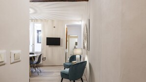 Une chambre d’hôtel dotée d’un téléviseur à écran plat fixé au mur, d’un coin repas avec une table et des chaises, et d’un espace détente avec un fauteuil et une lampe.