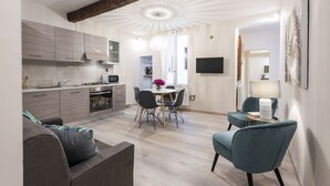 Une cuisine moderne avec des meubles gris, un coin repas avec une table ronde et des chaises, et un salon avec un canapé et un fauteuil bleu.