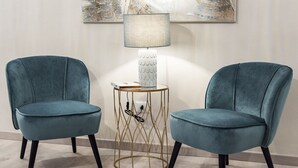 Deux fauteuils de couleur bleu sarcelle, une lampe blanche avec un abat-jour texturé et une table à structure en fil de fer doré.