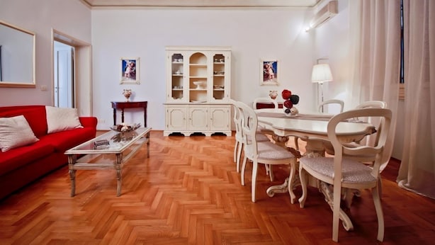 Una sala de estar con un sofá rojo, una mesa de centro, una mesa de comedor con sillas, un armario blanco y una lámpara.
