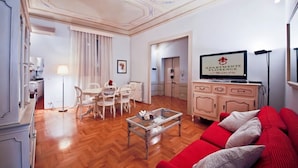 Una sala de estar con un sofá rojo, una mesa de centro de vidrio, un televisor y un comedor con sillas y una mesa.