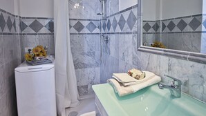 A bathroom with a white pedestal sink, a green sink, a shower, and a mirror with a decorative tile border. - Apartments Florence- Brunelleschi 1 bd (Firenze)
