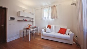 A living room with a white sofa, a dining table with chairs, a white cabinet, and a window with curtains. - Apartments Florence- Brunelleschi 1 bd (Firenze)