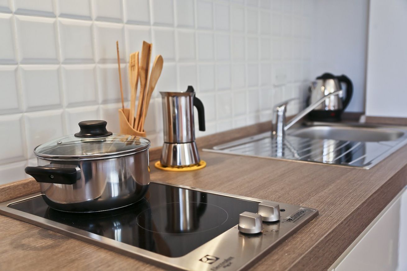 Eine moderne Küche mit integriertem Induktionskochfeld, einem Edelstahlkochtopf, einer Kaffeemaschine und Holzkocherutensilien auf der Arbeitsfläche.