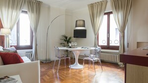 A modern room with a round dining table, clear chairs, a sofa, a floor lamp, and a TV mounted on the wall. - Apartments Florence- Santa Maria View (Firenze)