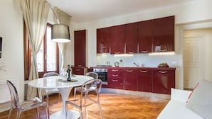 A modern kitchen with red cabinets, a white dining table, and a sofa. - Apartments Florence- Santa Maria View (Firenze)