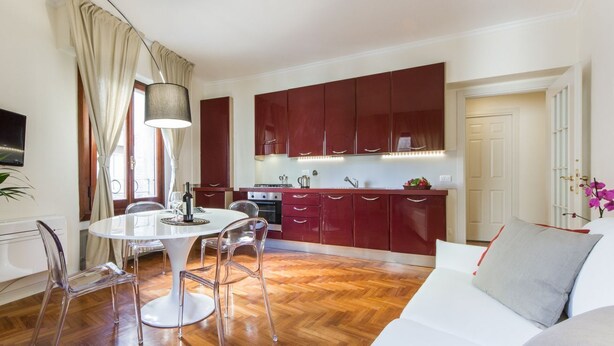 A modern kitchen with wooden cabinets, a dining table with chairs, and a living area with a sofa. - Apartments Florence- Santa Maria View (Firenze)