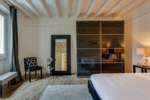 A hotel room with a bed, a chair, a small table with a vase, a mirror, and a wardrobe with a bed inside.