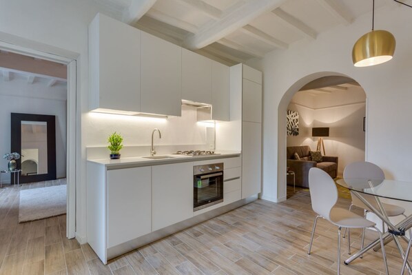 A modern kitchen with white cabinetry, a built-in oven, and a dining area with a glass table and chairs.