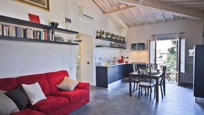 Ein Wohnzimmer mit einem roten Sofa, einem Esstisch mit Stühlen, einer Küchenzeile und einem Balkon.