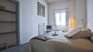 Ein Schlafzimmer mit Bett, Nachttisch, Fernseher, Heizkörper und einem Fenster mit Vorhängen.