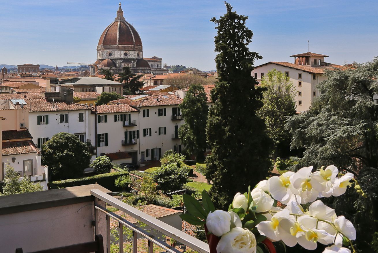 Une vue sur un paysage urbain avec un dôme imposant, des immeubles résidentiels et un balcon orné de fleurs.