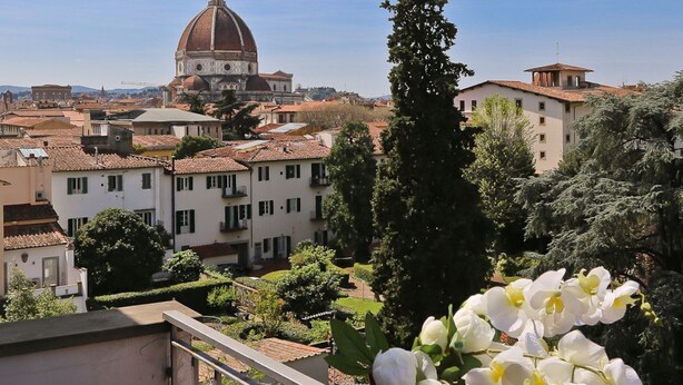 Blick auf eine Stadtlandschaft mit einer markanten Kuppel, Wohnhäusern und einem Balkon mit Blumen.