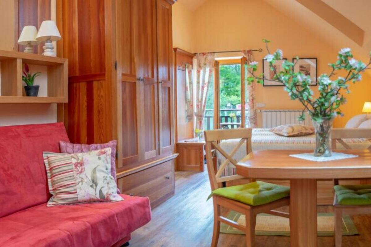 Une pièce chaleureuse avec un canapé rouge, des meubles en bois, une table à manger avec des chaises et une vue sur l’extérieur par une fenêtre.