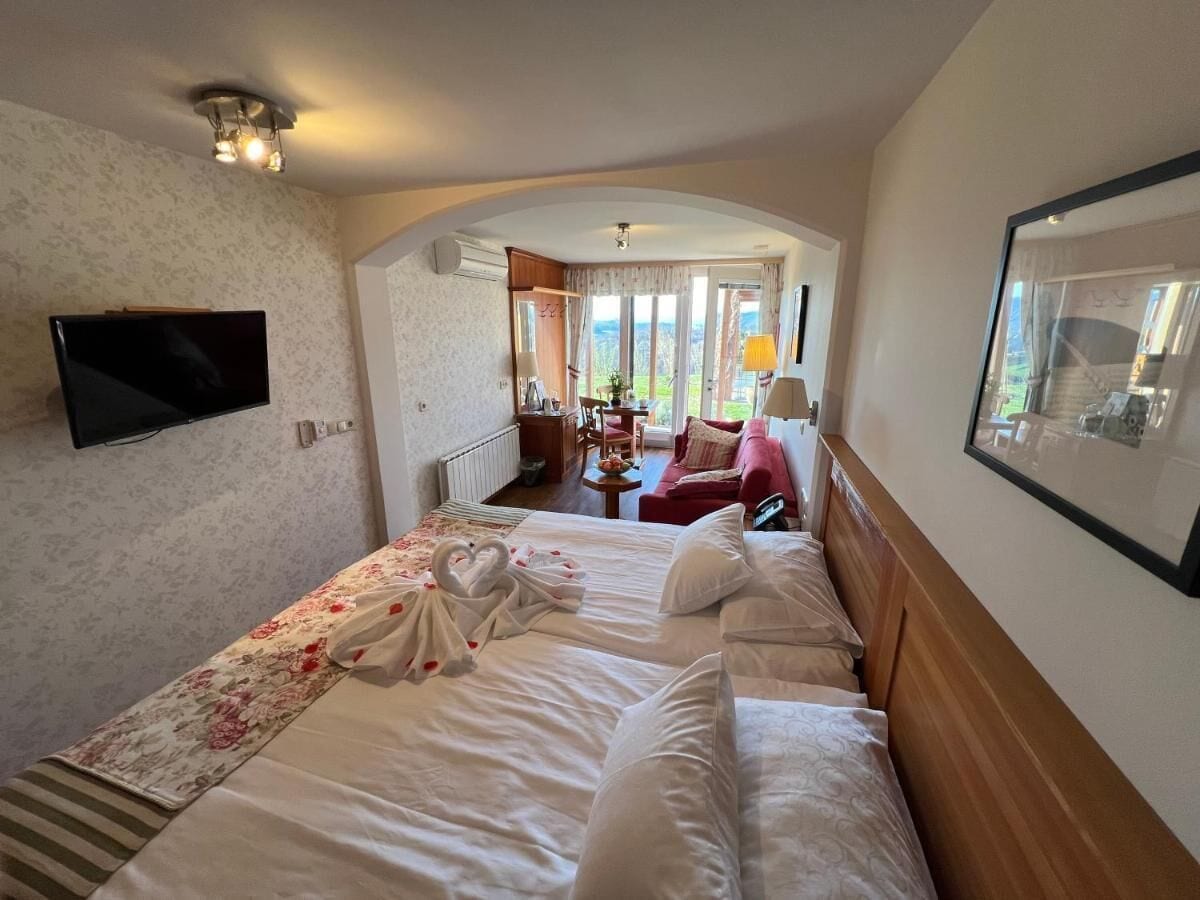 A hotel room with a large bed, a TV mounted on the wall, and a view of the outdoors through the window.
