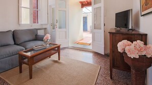 A living room with a sofa, a coffee table, a TV on a stand, and a door leading outside.