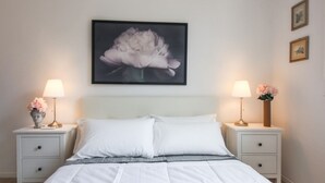 A bedroom with a bed, two bedside tables, a nightstand, a framed picture on the wall, and two lamps.