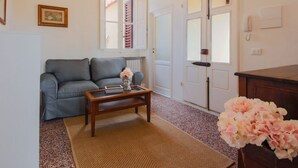 A living room with a grey sofa, a wooden coffee table, a patterned rug, a vase of flowers, and a door with a window.