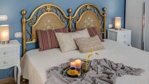 Una cama bien hecha con un cabecero decorativo, mesitas de noche con lámparas y una bandeja con velas y una taza.