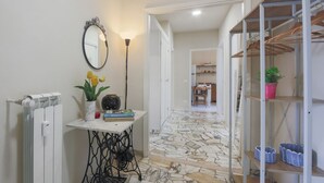A hallway with a radiator, a table with books and flowers, a mirror, and a patterned floor. - Apartments Florence- Rosselli Balcony (Firenze)
