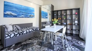 A modern living room with a sofa, dining table, chairs, a bookshelf, and a large painting of a seascape. - Apartments Florence- Rosselli Balcony (Firenze)