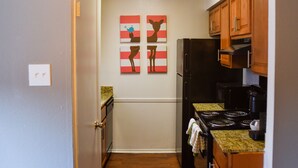 A compact kitchen with wooden cabinets, a black refrigerator, a stove, and two wall-mounted artworks. - 6 Mins Away Cowboy/Ranger Stadium Arlington 1bd (Arlington)
